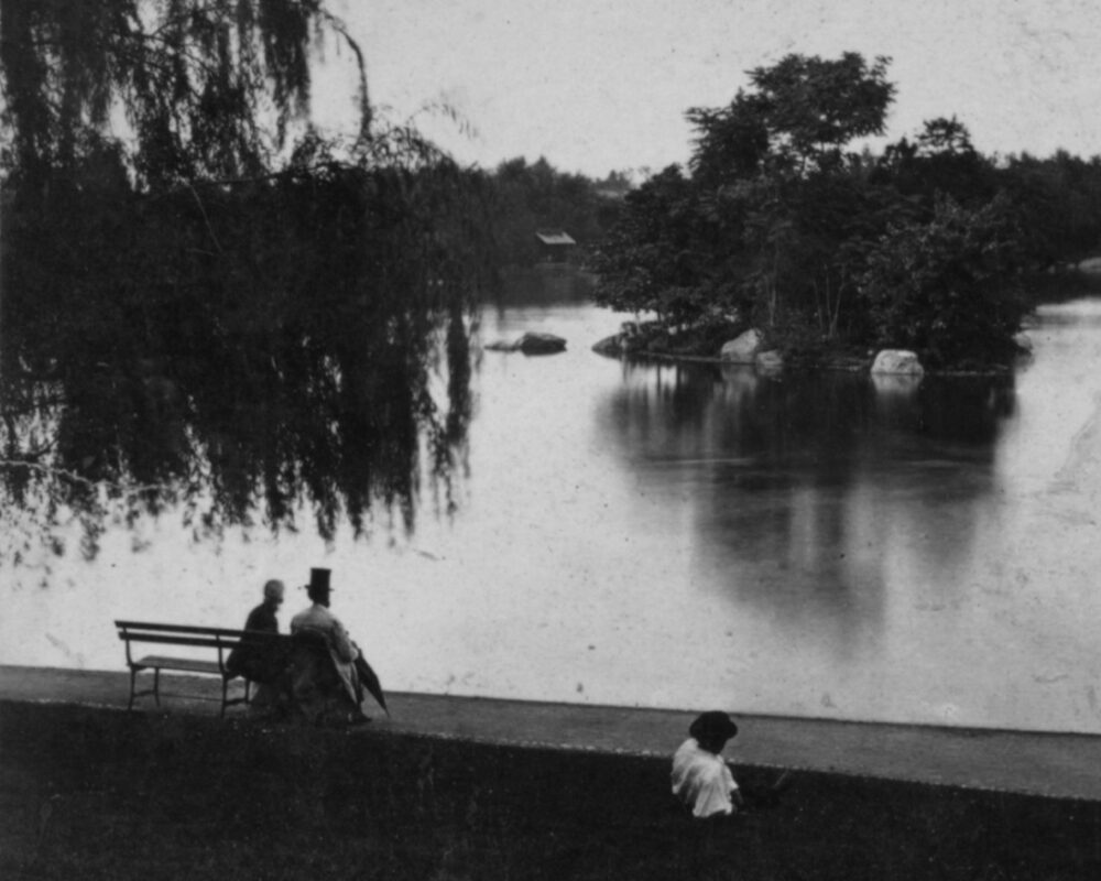 Antique photo showing a couple on a bench by the Lake, with the gentleman wearing a top hat