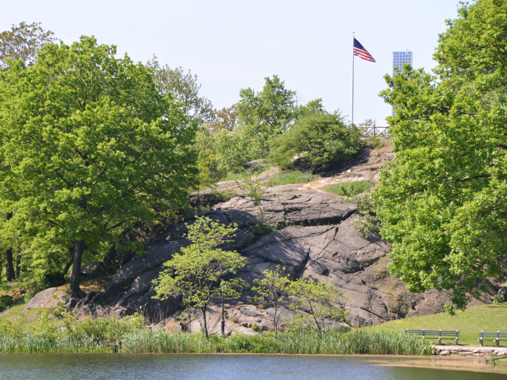 Bedrock and green trees of the Fort Landscape in the northern part of Central Park, with a US flag in the background
