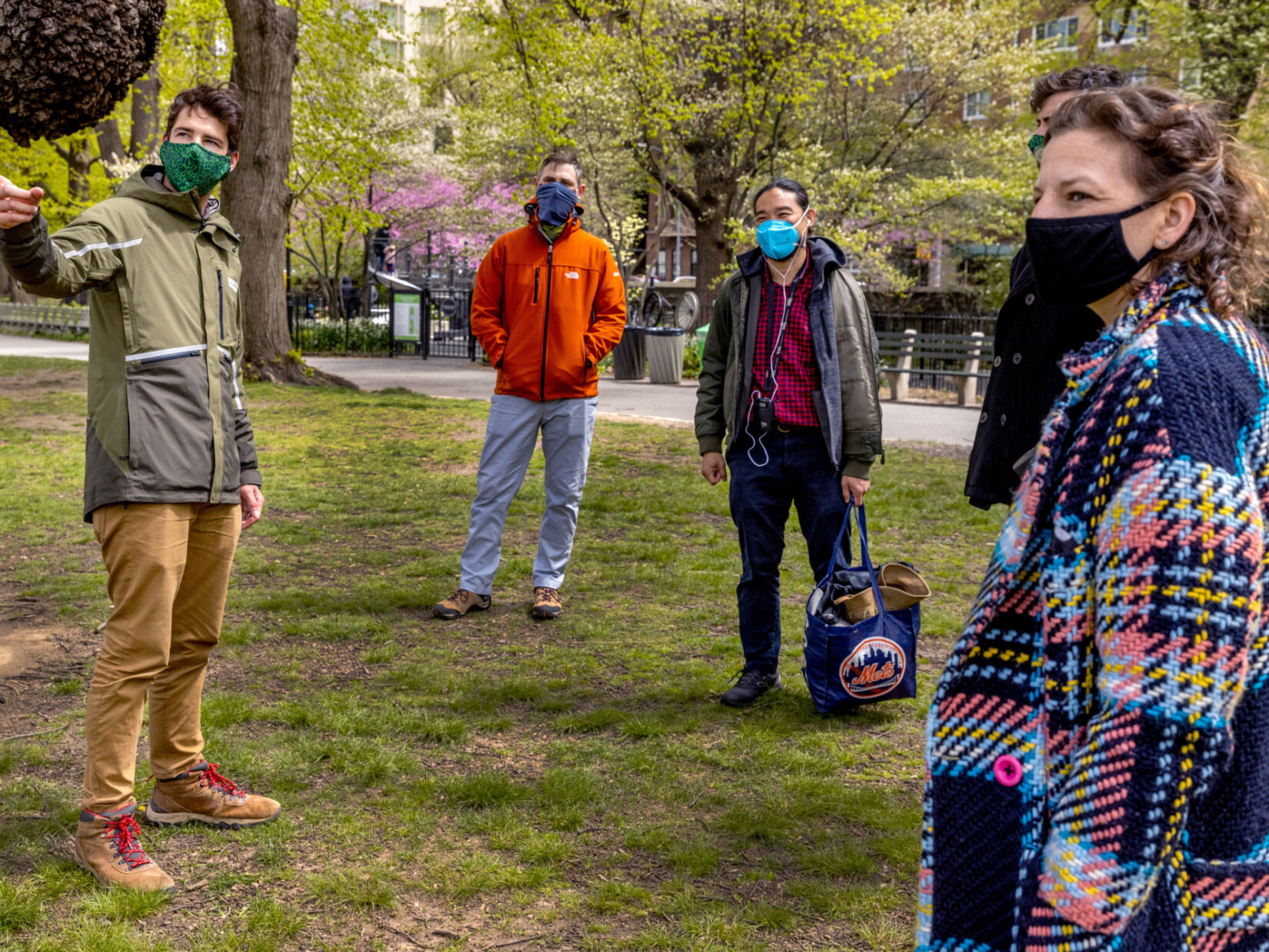 A tour guide wearing a green jacket shows a group of people around Central Park