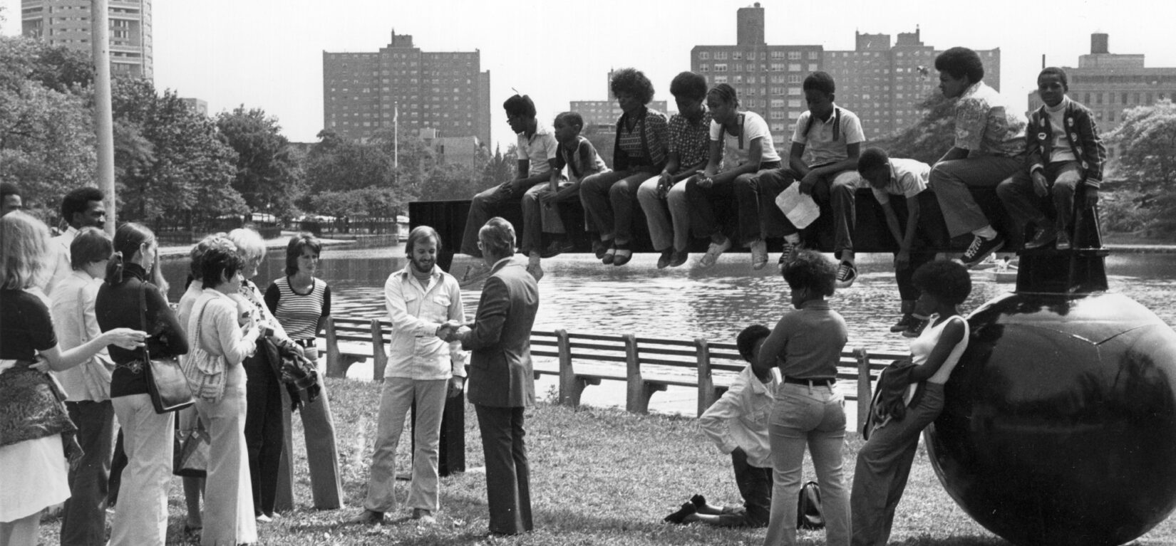 A black and white photo of the sculpture on the banks of the Meer, with people surrounding and sitting on top of it.
