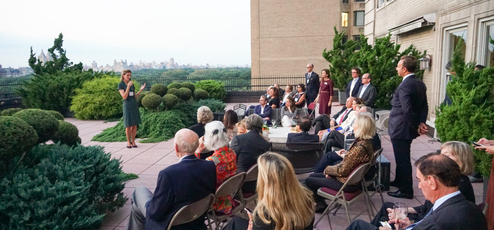 Betsy Smith addressing guests on a rooftop over looking Central Park