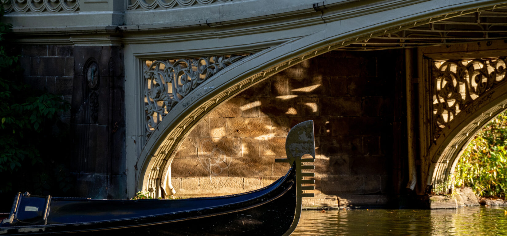 A boat sails under Bow Bridge in Central Park during sunset