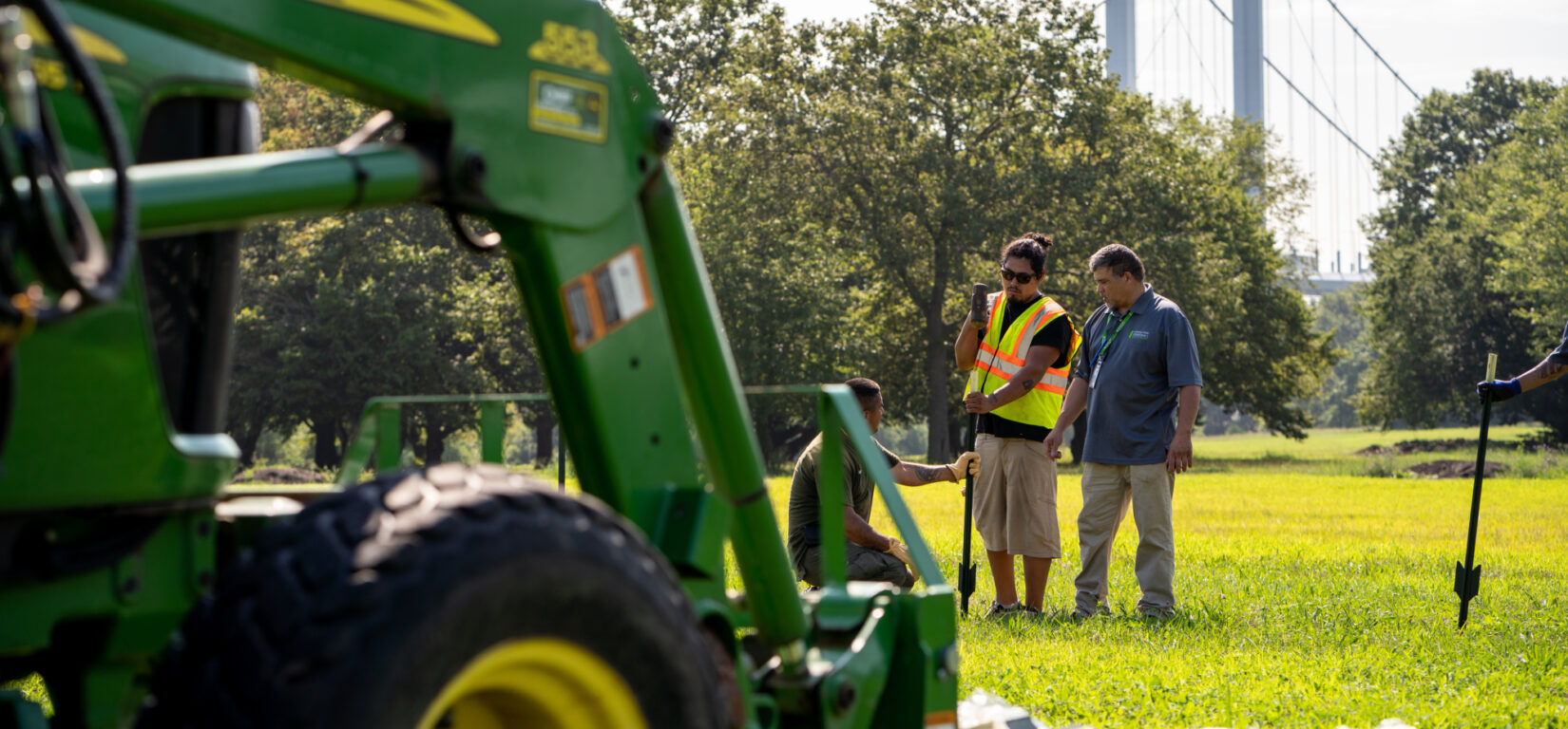 Park staff working at Ferry Point Park, with the Throgs Neck Bridge in the distance