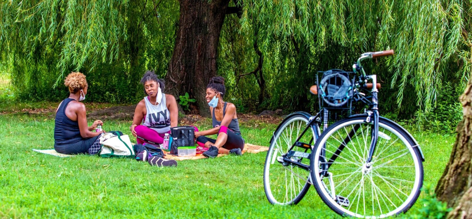 Three women enjoy a picnic on a blanket on Cedar Hill, with a parked bicycle in the foreground.