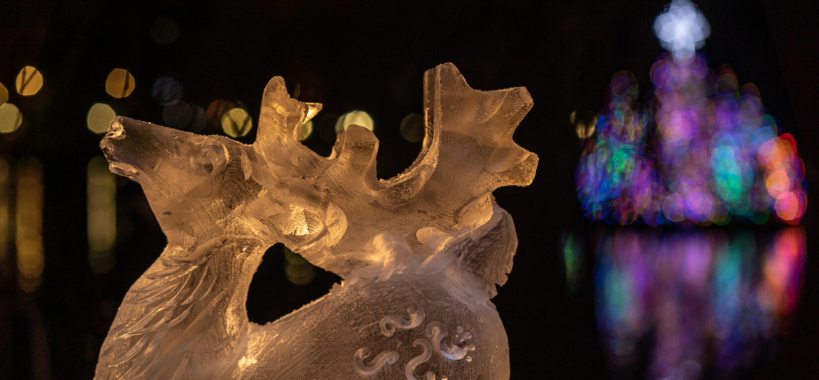 An ice carving of a reindeer is backlit on the banks of the Meer at night