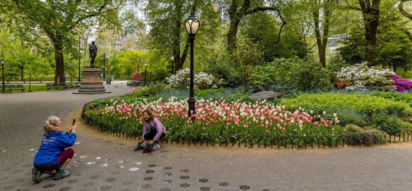 A woman kneels to pose in front of the flower bed