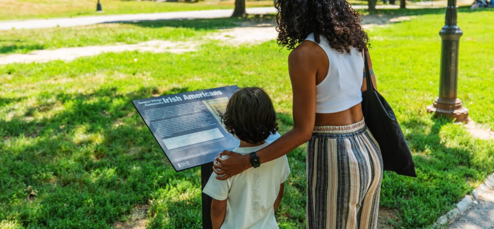 A woman and a child reading one of the in-Park signs describing Seneca Village