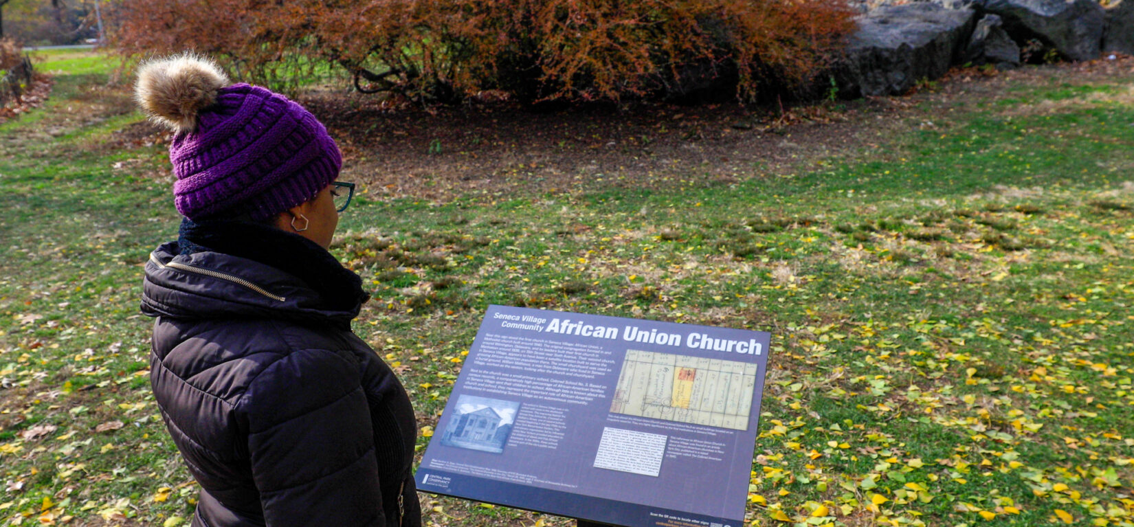 A woman reads an informational sign about Seneca Village
