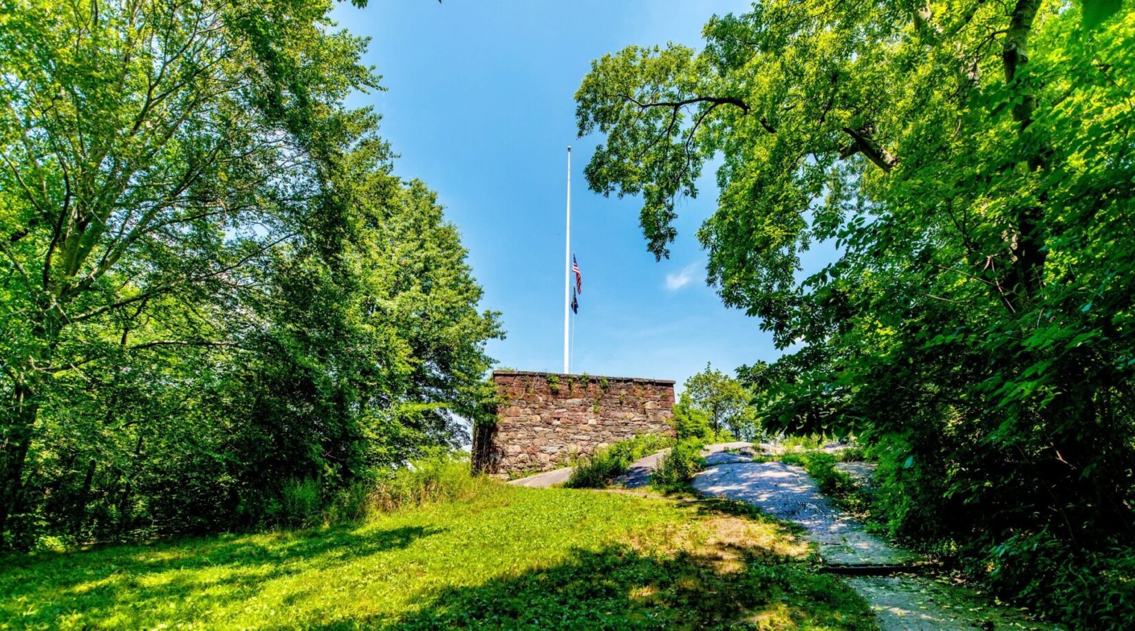 A view looking up the hill to the Blockhouse, topped with a white flagpole and a flag at half mast.
