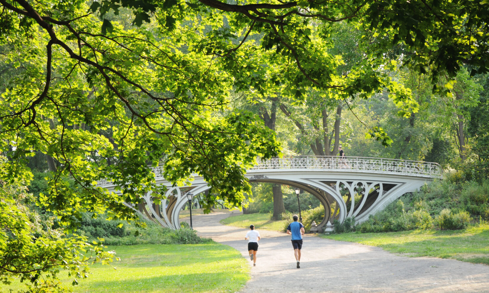 A pair of joggers on the bridle path head under Bridge 28 and a canopy of spring-green trees.
