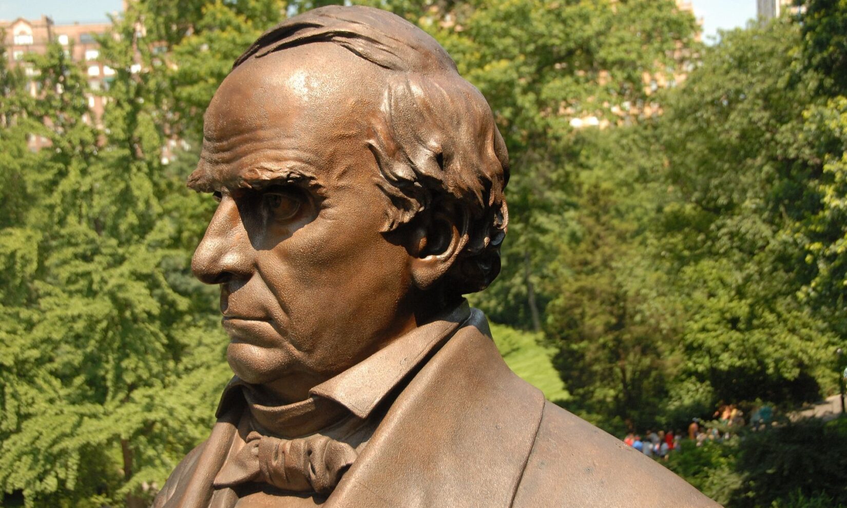 A closer view of Webster's profile against a blue sky and greenery.