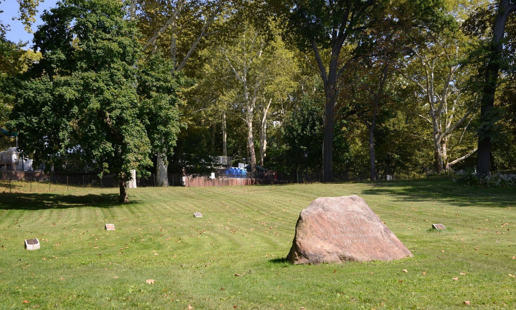 The memorial grove is bathed in sunlight, dotted with small plaques and a prominent stone.