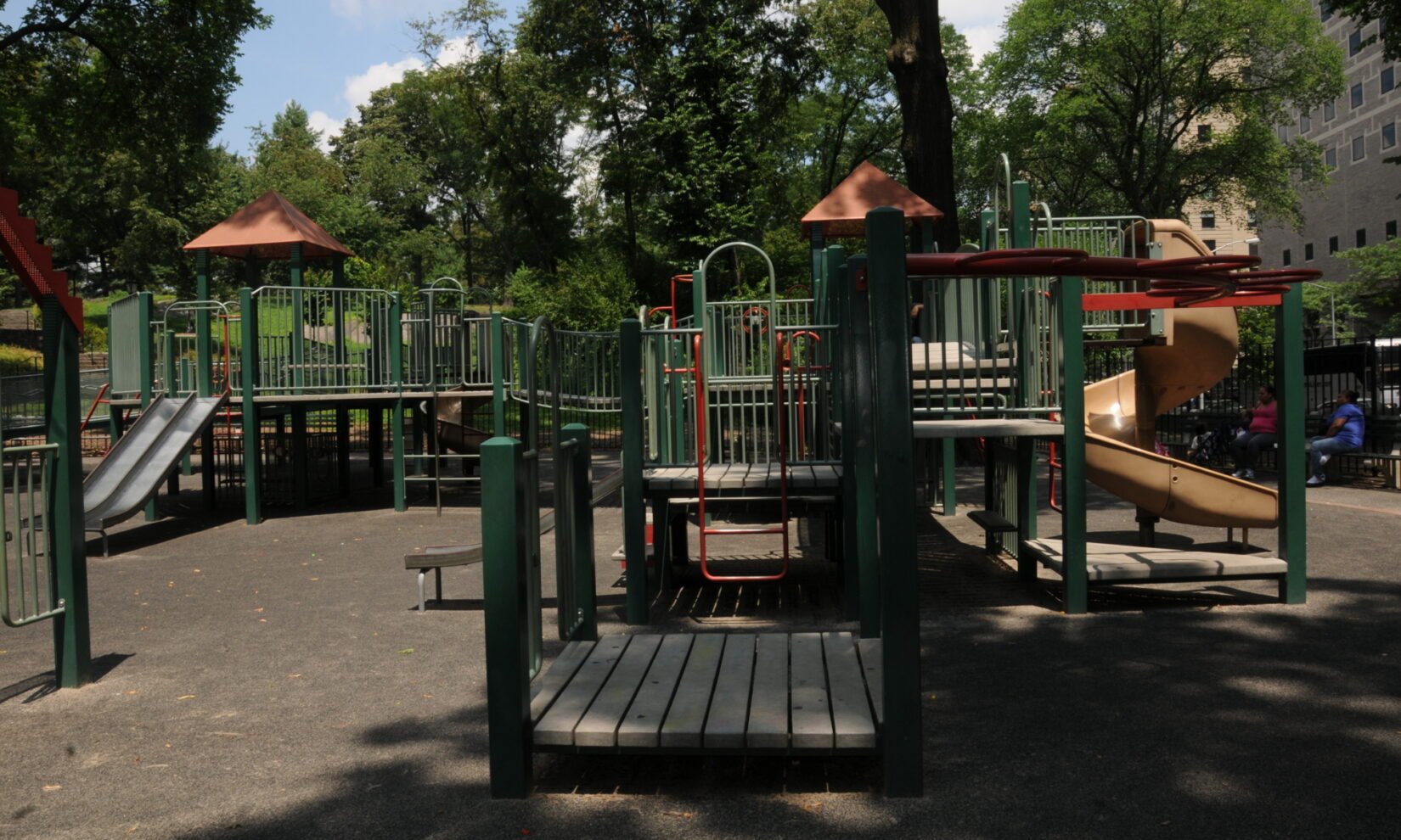 Several sets of climbing equipment are ringed by summer trees.