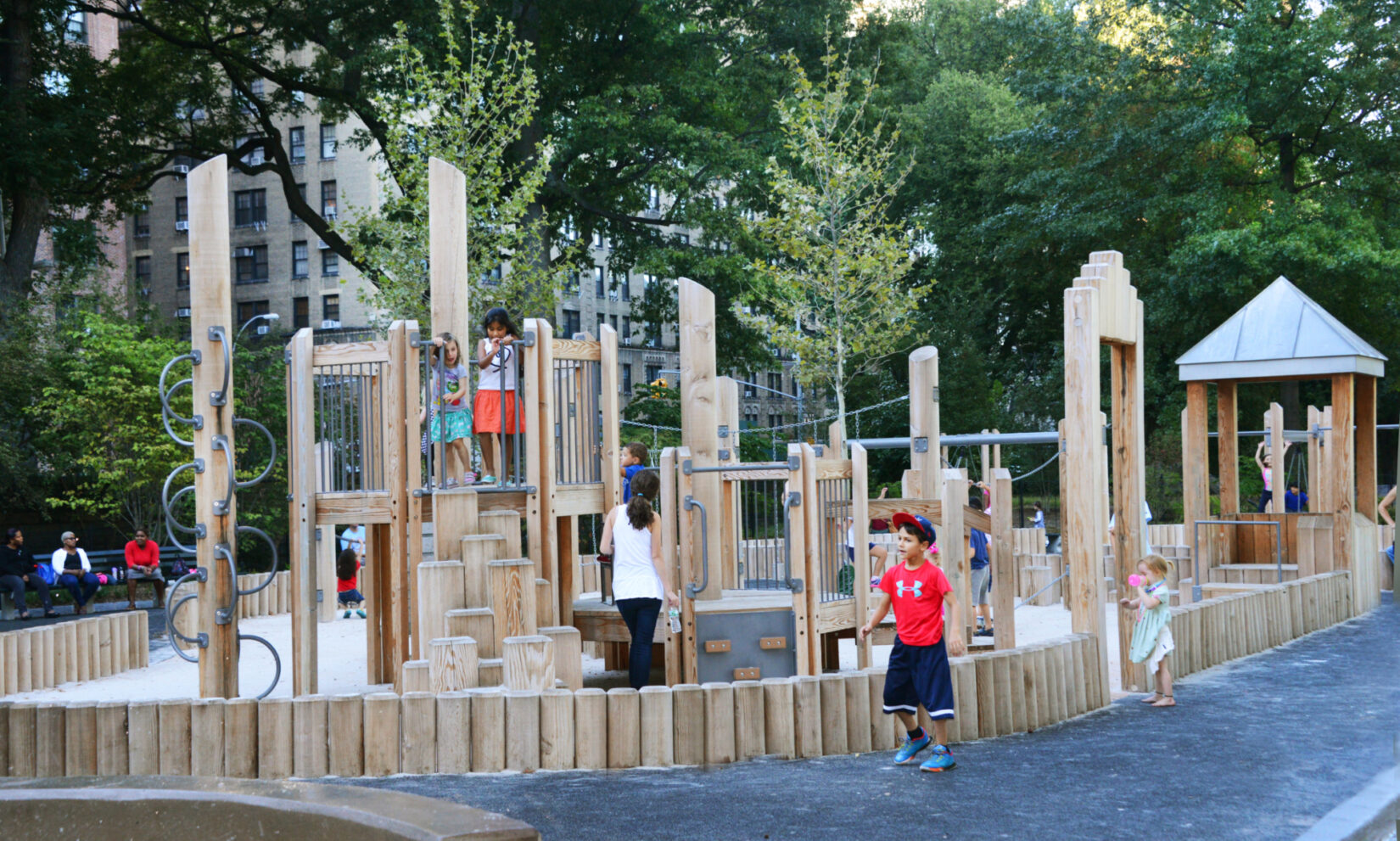 Wooden play structures surround sandy ground, surrounded by a path.